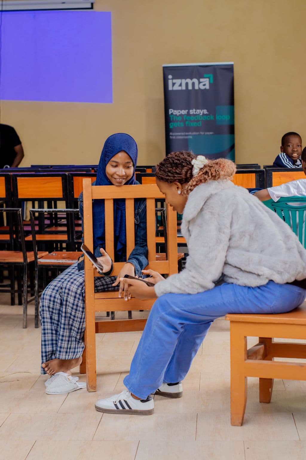 Two people sitting together and looking at their phones in a classroom
